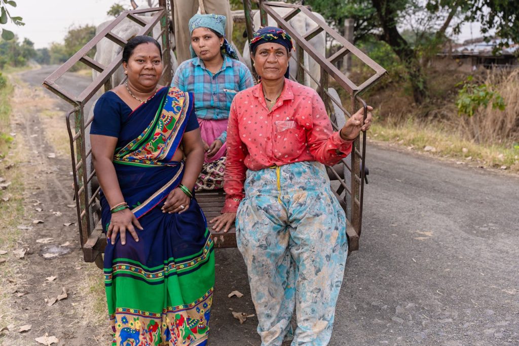 Three women farmers in traditional attire pose on a rural path in Nagpur, India.