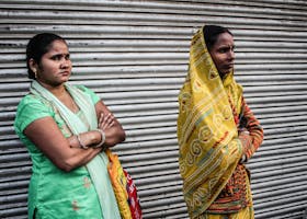 Two Indian women wearing traditional sarees stand outdoors, showcasing cultural attire and expressions.
